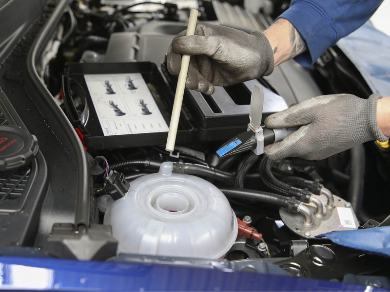 bremsfluessigkeit-wechseln.jpg Motorraum eines Autos, bei dem Bremsflüssigkeit nachgefüllt wird